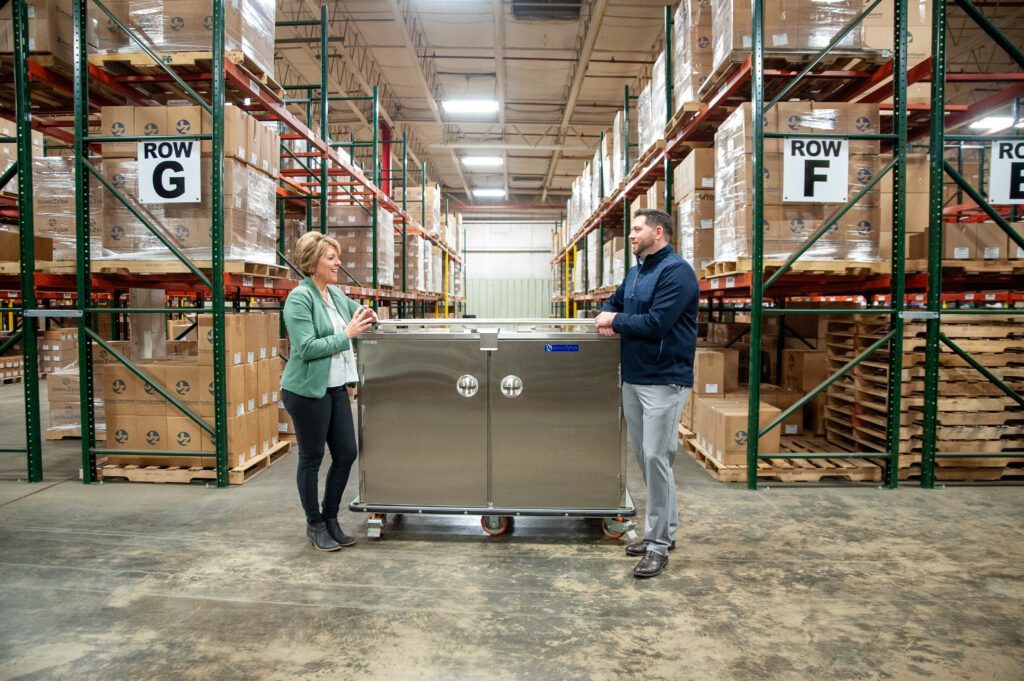 A woman and a man stand next to a piece of metal cabinetry in a warehouse