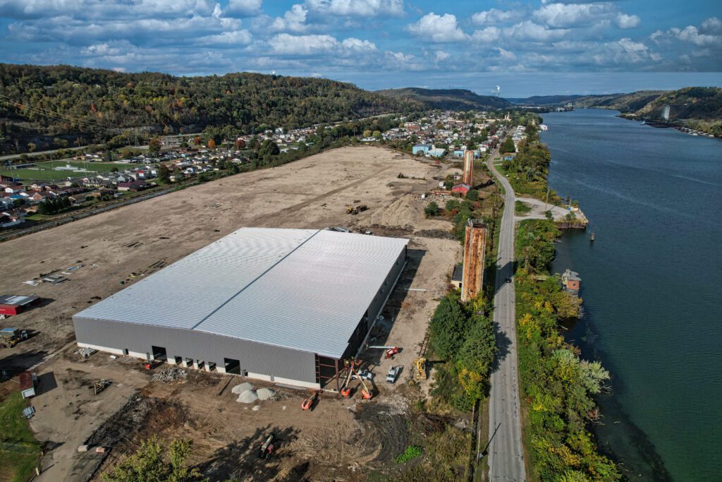 A drone image of a large metal building newly constructed on a site next to a river