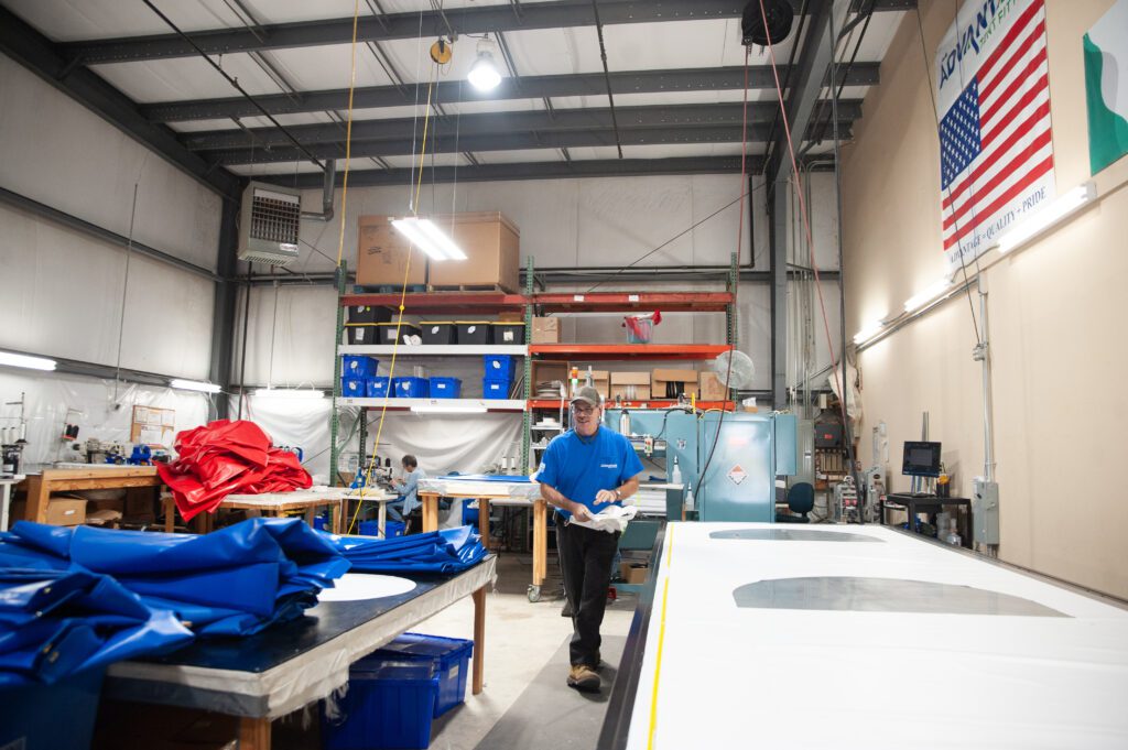 A man stands in the center of a manufacturing facility with blue tarps to his left